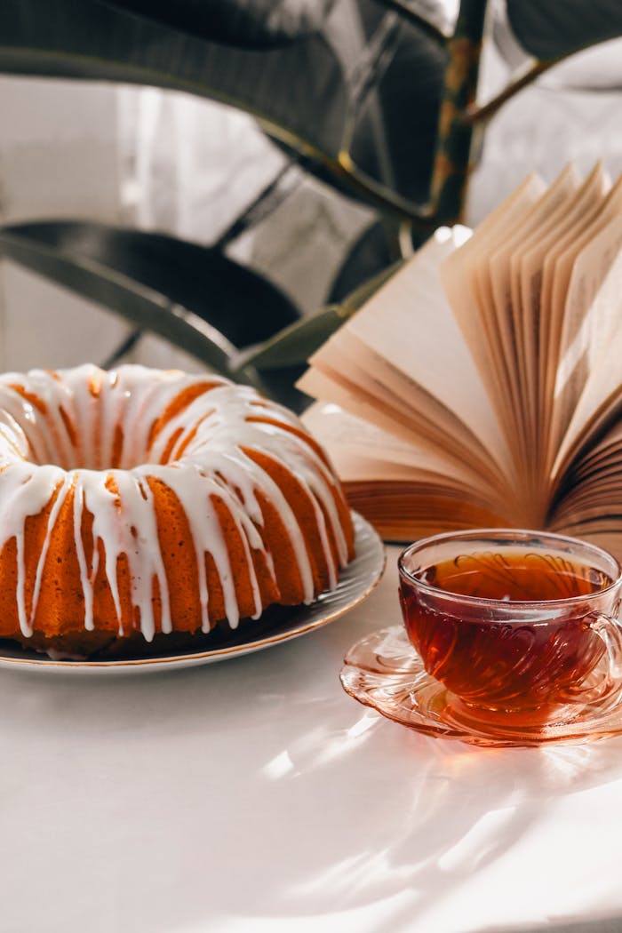 our-services-2 Delightful bundt cake with white icing paired with a cup of tea and an open book in a warm setting.