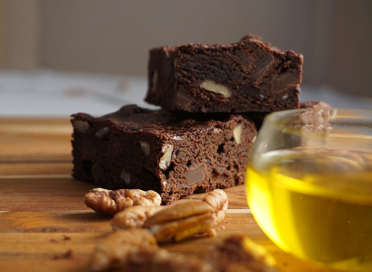 gallery-1 Close-up of chocolate brownies with nuts beside a cup of tea on a wooden table.