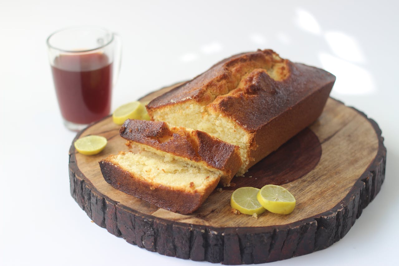 gallery-2 Freshly baked lemon cake with a cup of tea, beautifully presented on a rustic wooden board.